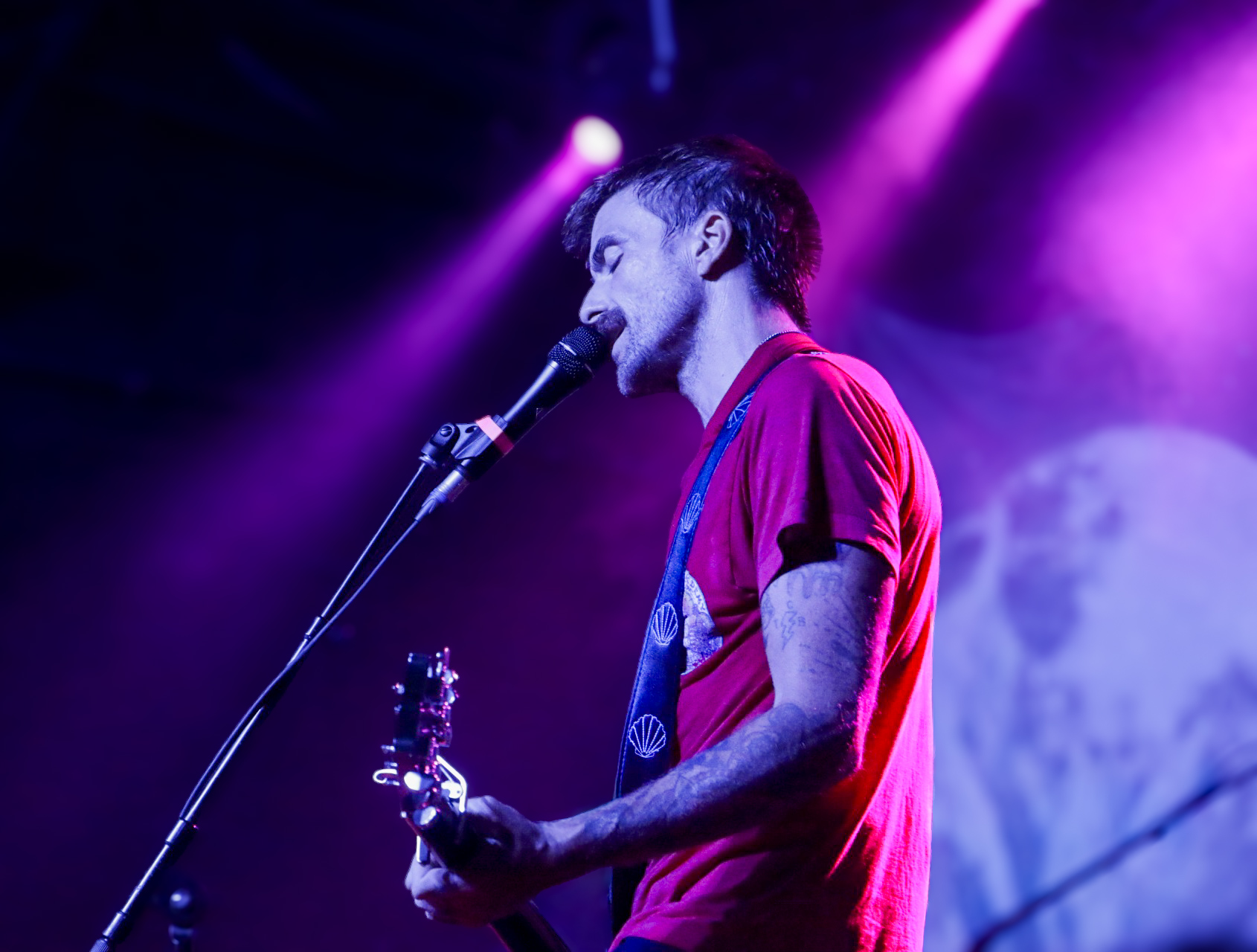 Musician singing into a microphone under purple stage lights