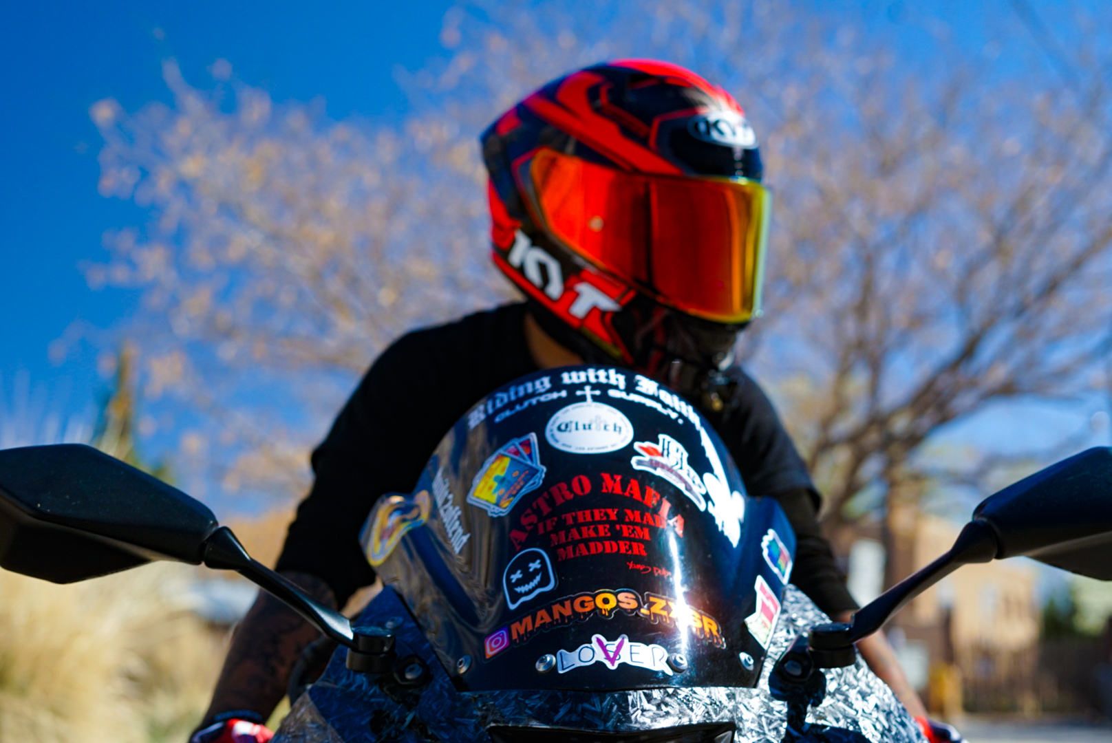 Rider in a red and black helmet behind a sticker-covered motorcycle windscreen