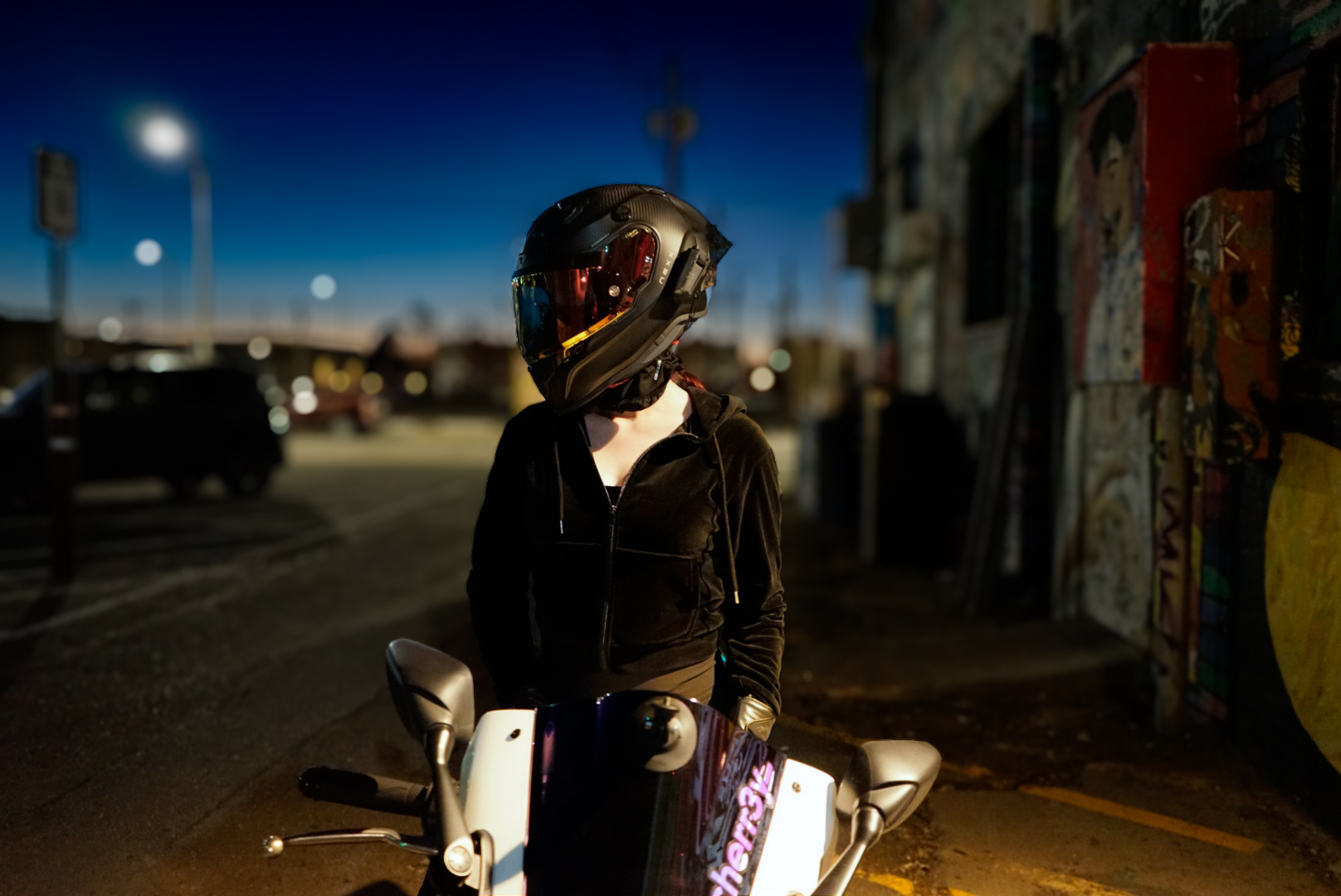 Rider in a black full-face helmet and dark hoodie on a scooter at night