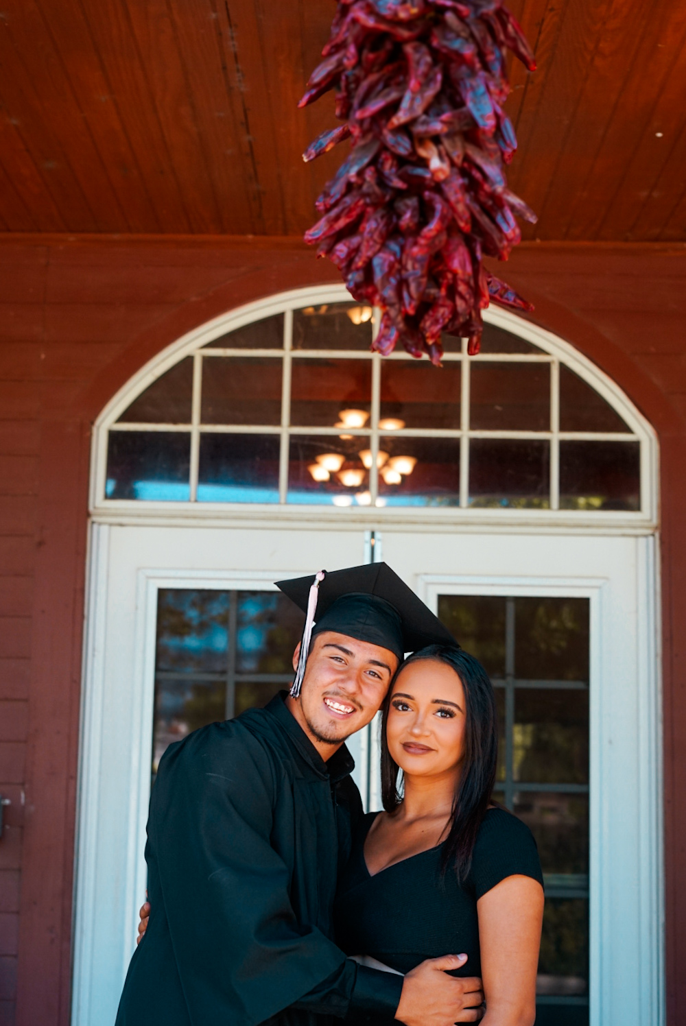 Graduating couple embracing in front of a red building from The Eclipse session
