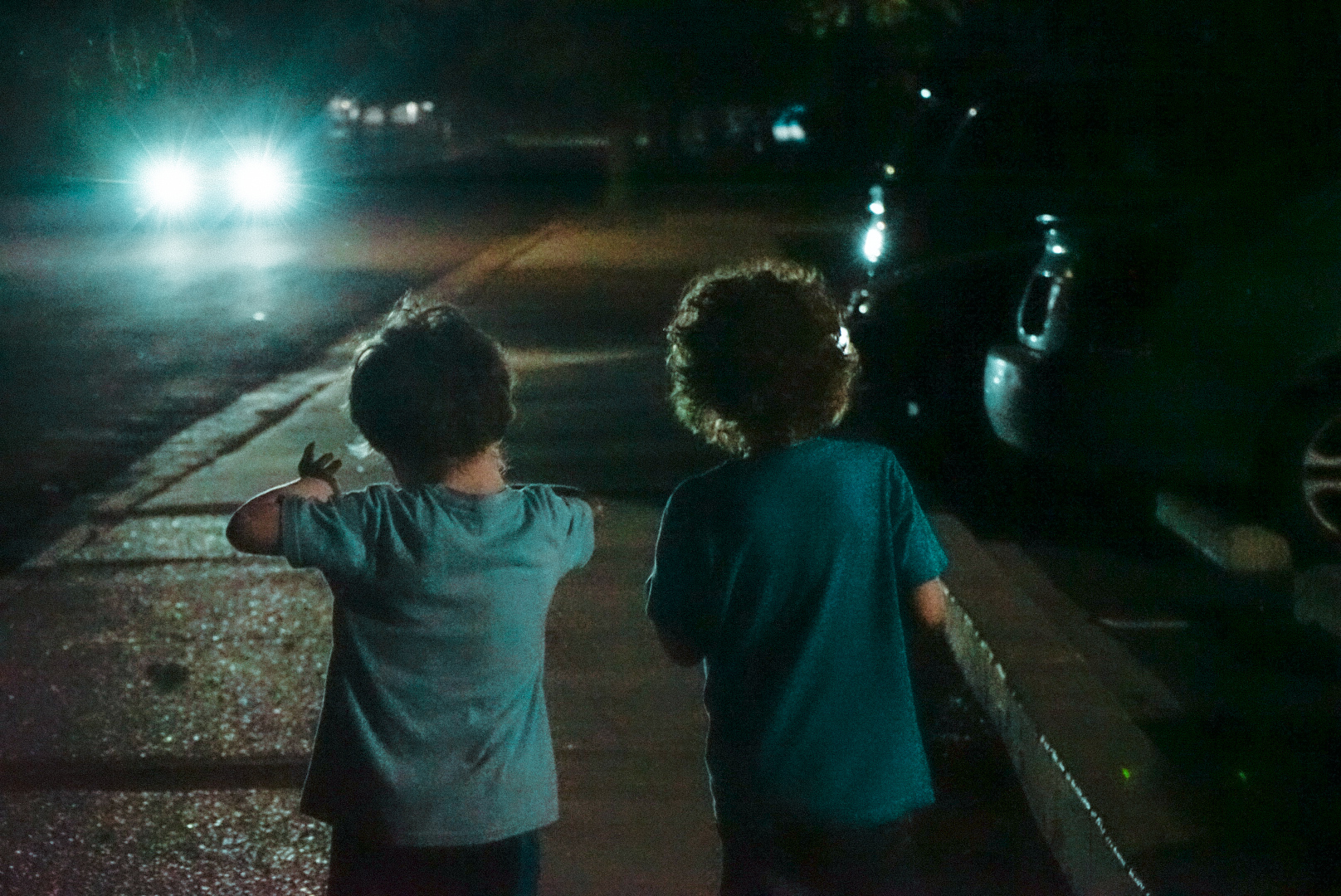 Two children walking toward bright headlights on a dark street