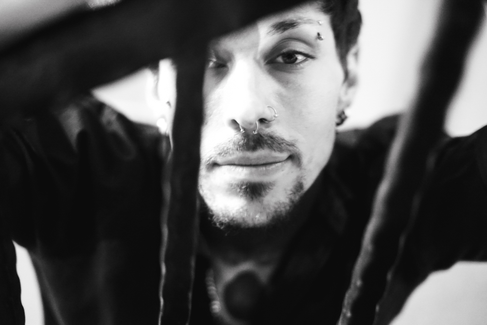 Black and white close portrait of a man with piercings behind hanging straps