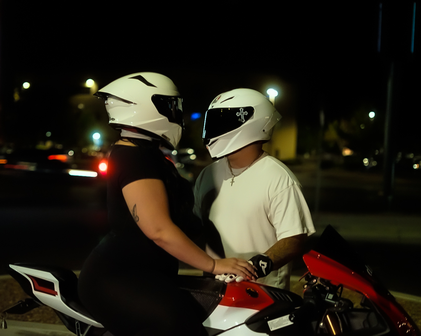 Two riders in white helmets beside a red sport bike at night