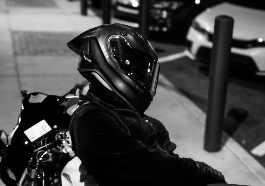 Black and white profile of a rider in a full-face helmet next to a motorcycle
