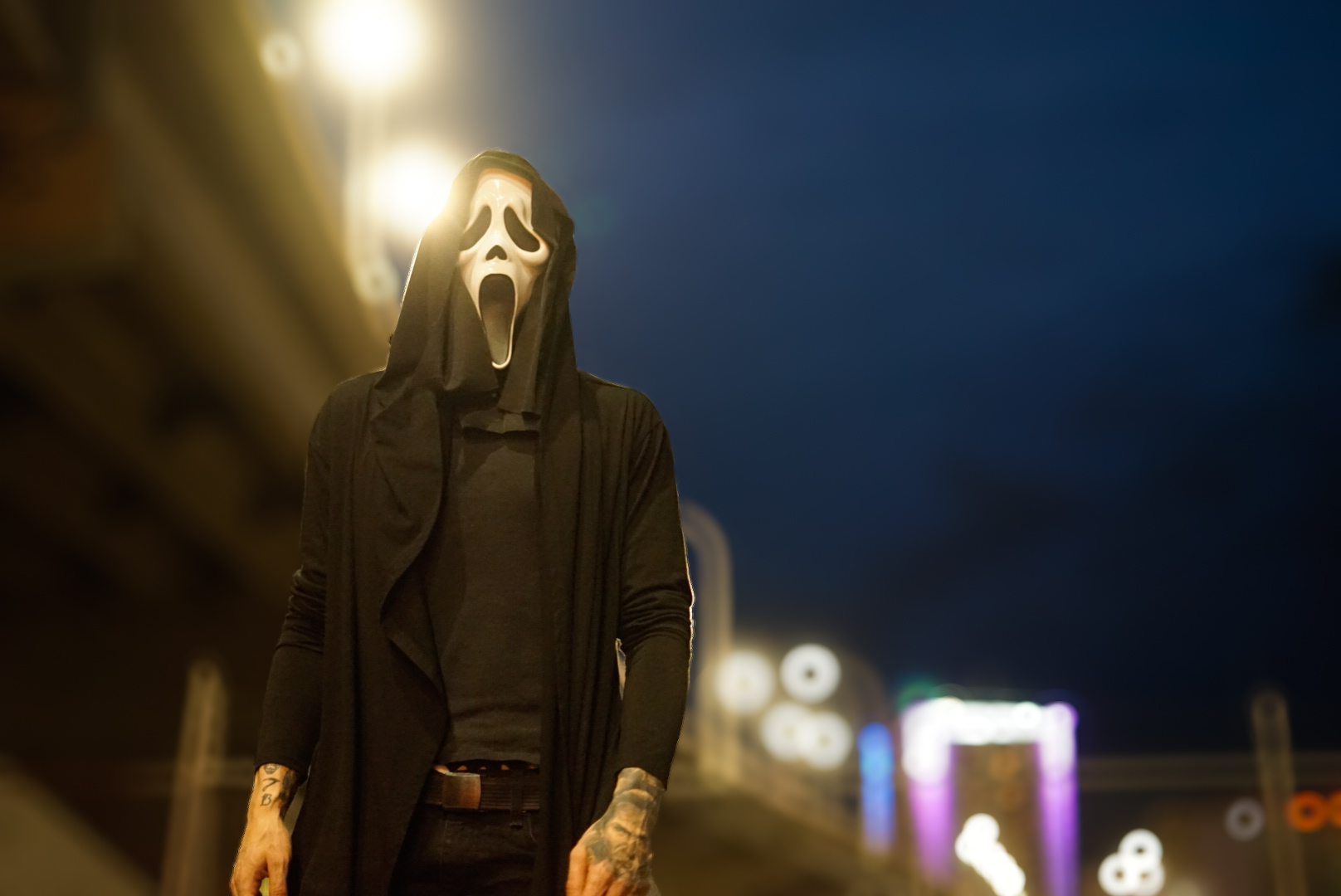 Person in a Ghostface mask and black robe under a bright streetlight at night