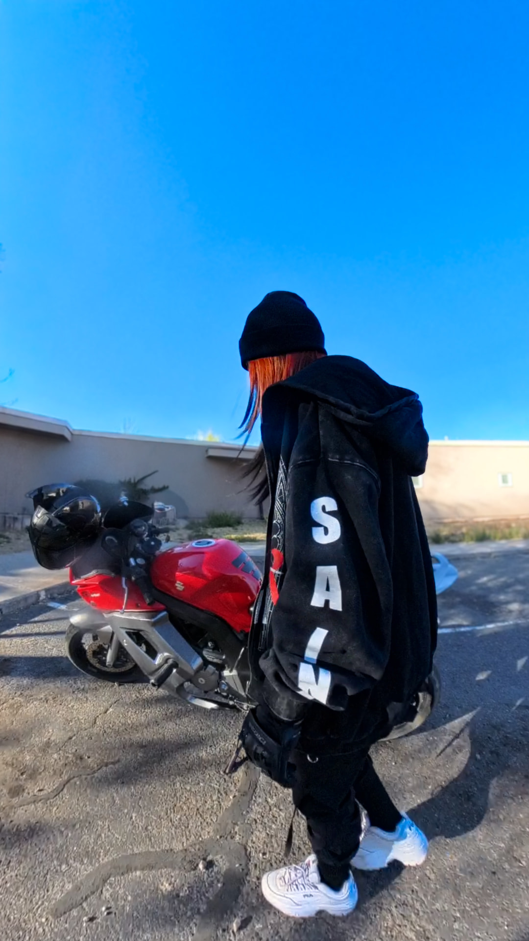 Person in a black beanie and jacket walking toward a red sport bike