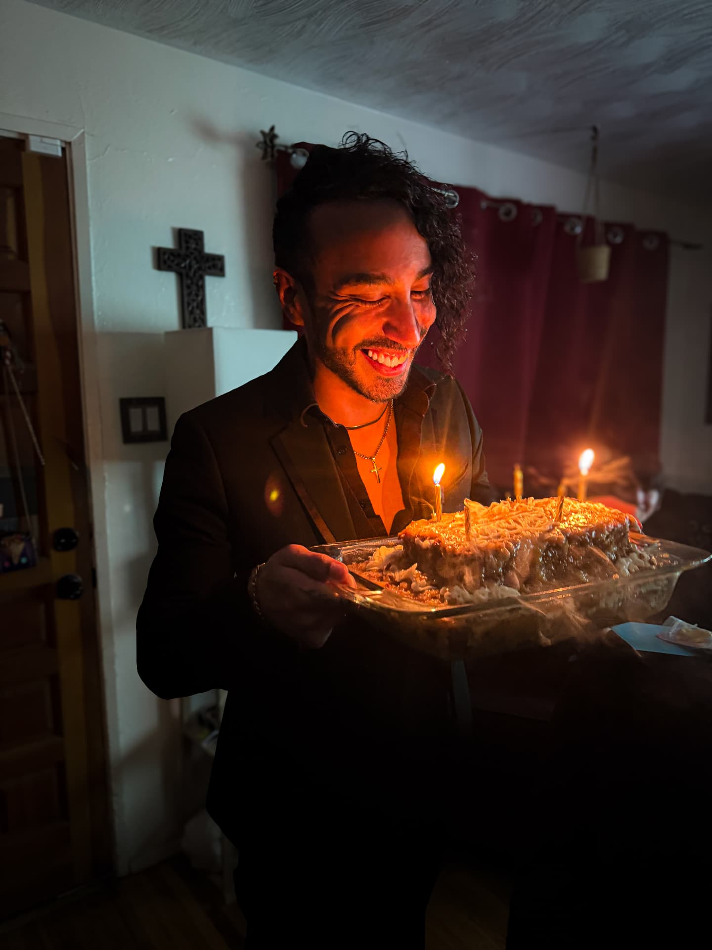 Person smiling while holding a birthday cake lit by candlelight