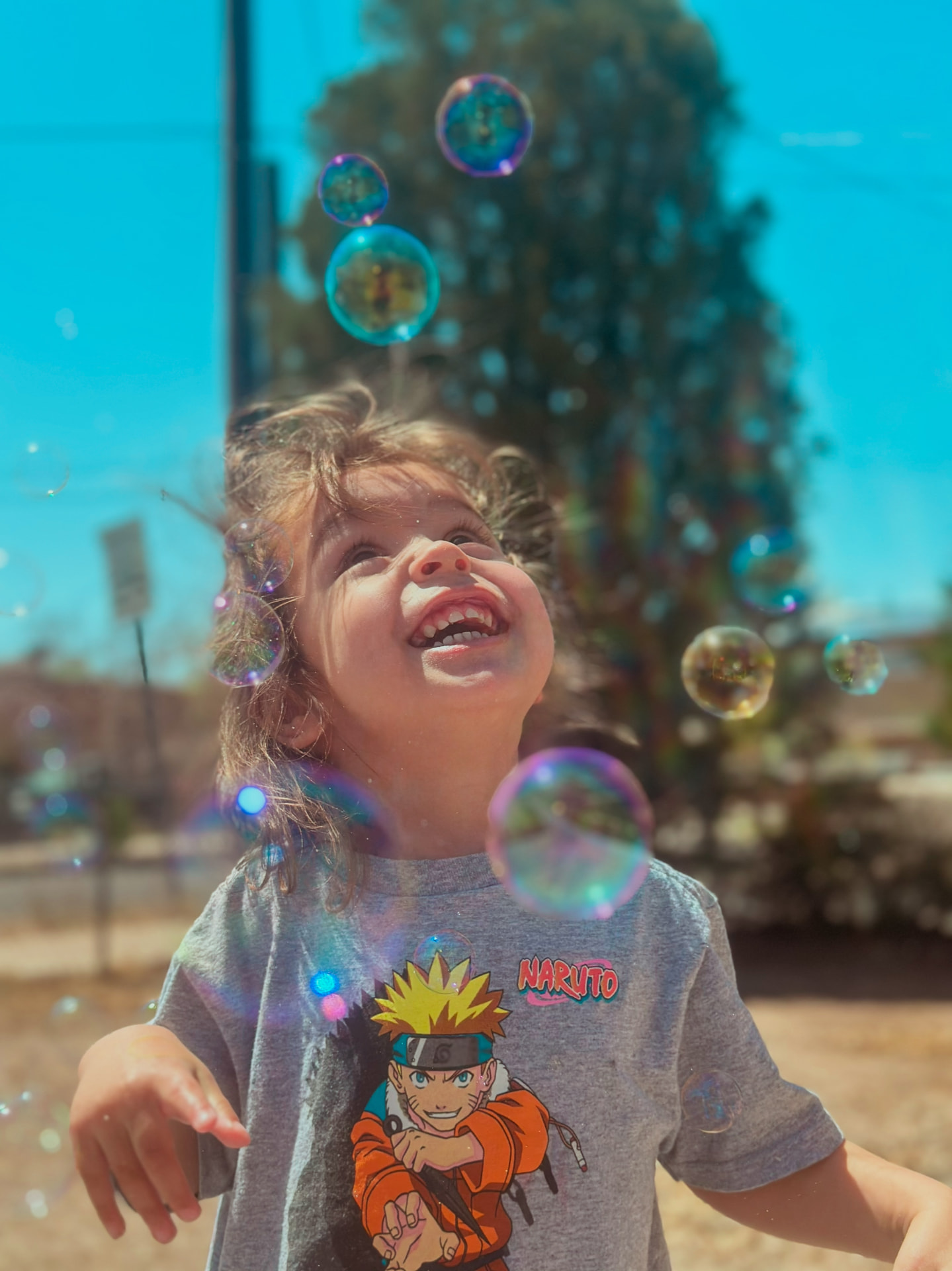 Child smiling up at floating soap bubbles on a sunny day